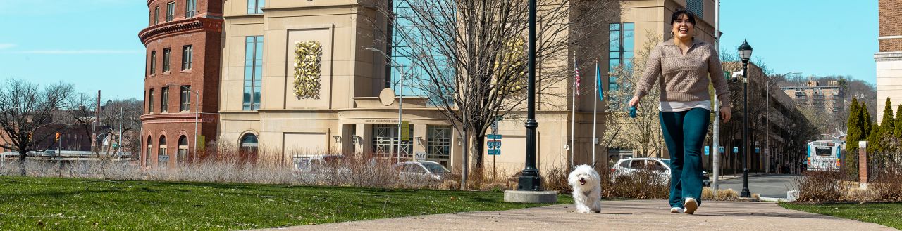A smiling, young woman walking her dog outside in downtown Waterbury