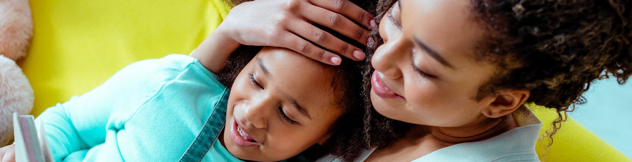 A mother holding her daughter close and smiling, with her hand on her daughter's forehead