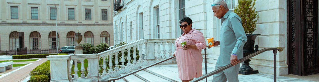 Woman and man walking down Waterbury City Hall steps together, outdoors, with healthy juice drinks in hand