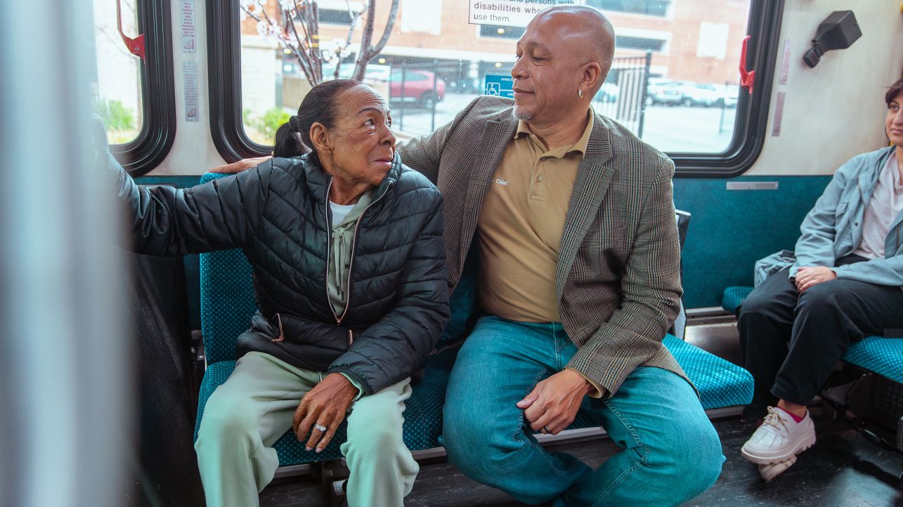 Man and his senior mother sitting on a public bus in Waterbury together, looking at each other and smiling