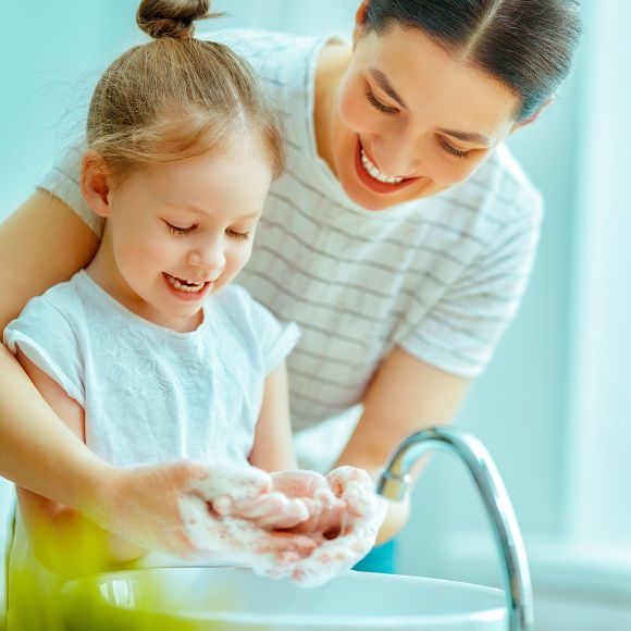 Woman helping her young daughter wash her hands at the sink