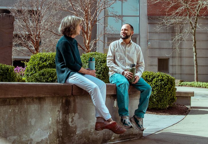 Two people sitting on a stone bench in downtown Waterbury, talking with each other