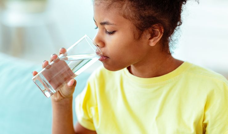 A young person taking a sip of water from a glass