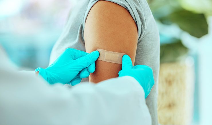 A shot of a doctor's gloved hands, putting a band aid on a patient's arm