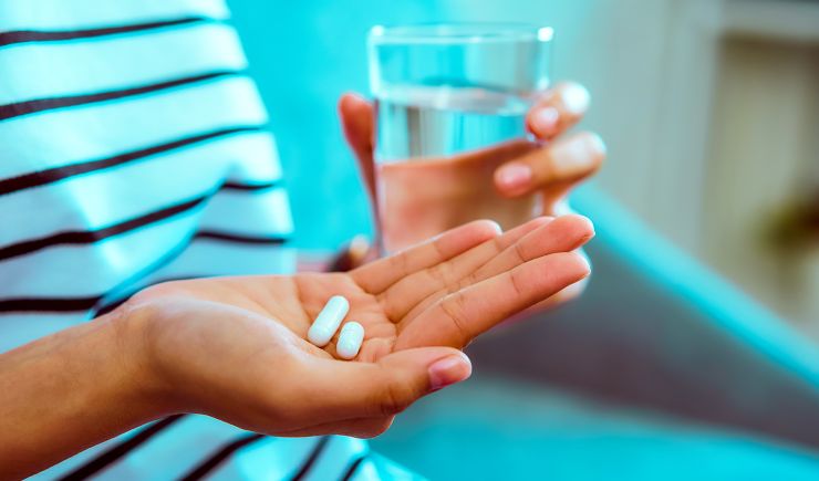 Shot of a person's hands holding two tablets of medicine and a glass of water