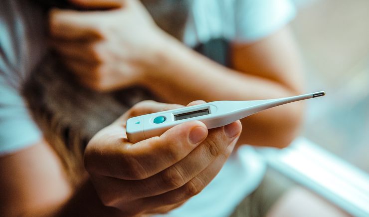 Shot of a person's hands holding a thermometer, checking their temperature