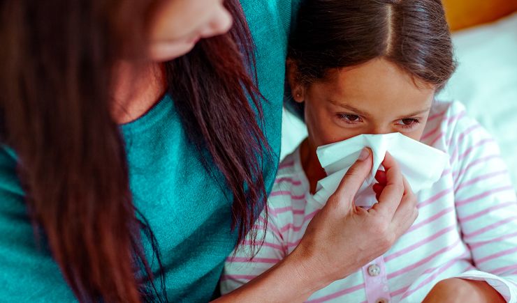 Mother helping her young daughter blow her nose in a tissue