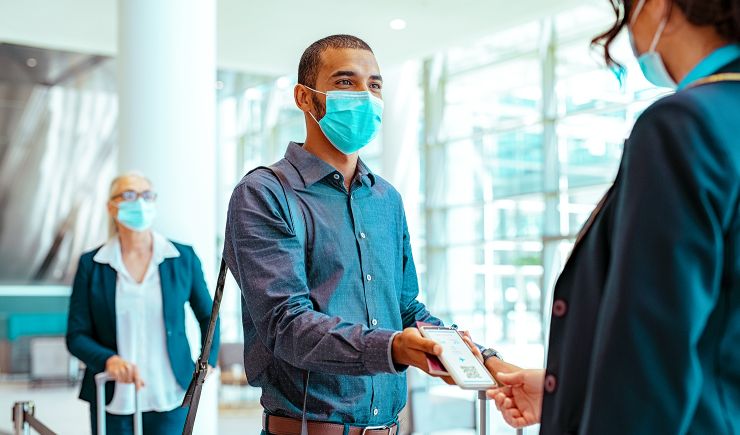 Masked man in airport showing ticket on phone to worker at gate