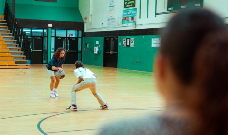 Mother watching daughter and classmate play basketball in school gym