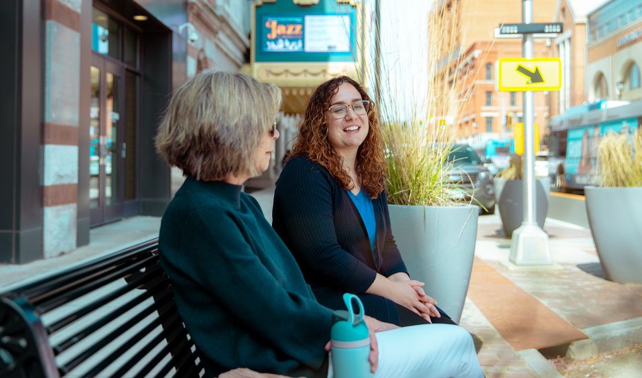 Two women sitting on a bench outside of the Palace Theater in Waterbury, smiling and talking