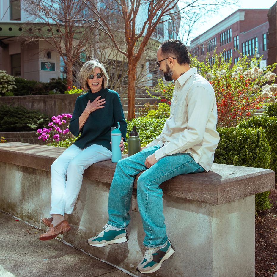 Man and a woman sitting on a stone bench in downtown Waterbury, laughing together